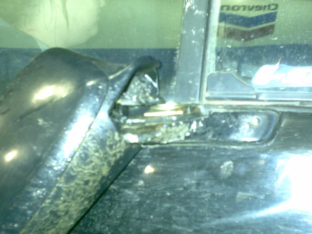 Keys hanging from the door lock of a dark vehicle with a Chevron sign reflected in glass