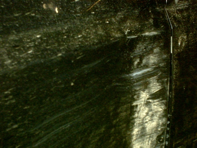 Close-up of a scratched, swirled dark green vehicle body panel and door seam