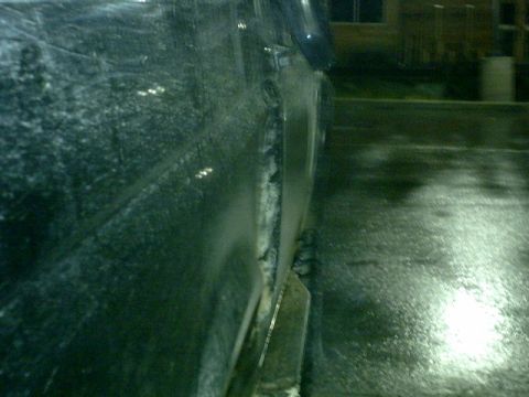 1995 Ford Bronco - Side profile of a dark SUV covered in mud splatters, seen from a low angle on a wet surface.