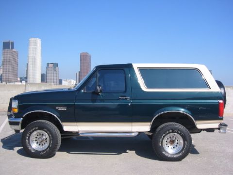 1992 Ford Bronco - Side profile of a two-tone 1992 Ford Bronco parked outdoors with a city skyline in the background.