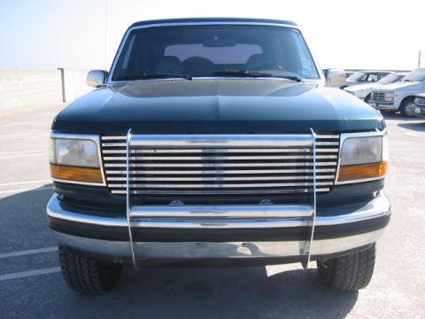 1992 Ford Bronco - Front view of a dark green 1992 Ford Bronco with a chrome grille and bumper, parked in a lot with other vehicles visible.