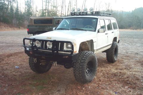 1987 Ford Bronco - A modified Jeep Cherokee XJ is parked outdoors with another vehicle in the background.