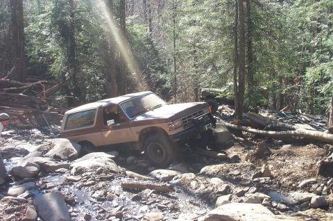 1987 Ford Bronco - This 1987 Ford Bronco is shown off-roading through a rocky stream in a wooded area.