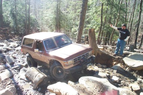 1987 Ford Bronco - 1987 Ford Bronco tackling rough terrain in a wooded area.