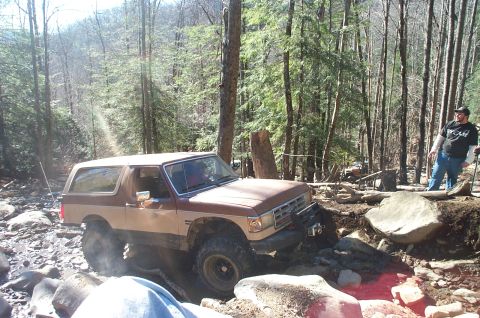 1987 Ford Bronco - This SUV is navigating a difficult, rocky trail in a wooded area.