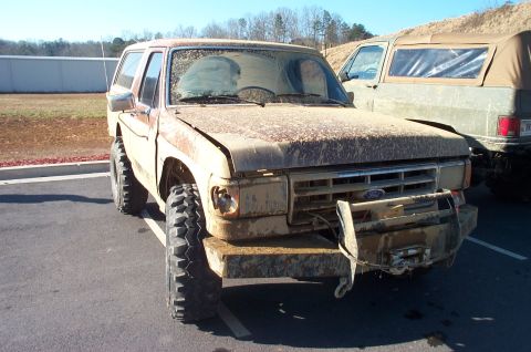 1987 Ford Bronco - This heavily mud-caked 1987 Ford Bronco sits parked, showing off its off-road tires and front winch.