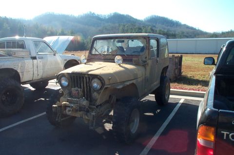 1987 Ford Bronco - A weathered Jeep CJ-5 sits parked in a lot, accompanied by other vehicles under a bright sky.