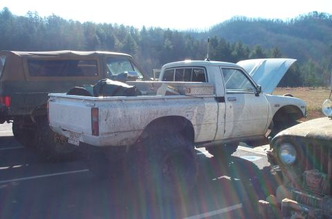 1987 Ford Bronco - Multiple vehicles parked outdoors with a wooded hillside in the background.