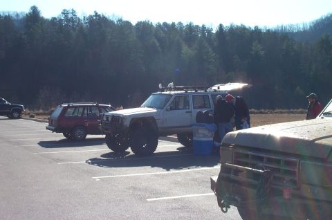 1987 Ford Bronco - A modified white Jeep Cherokee XJ is parked in a lot with other vehicles.