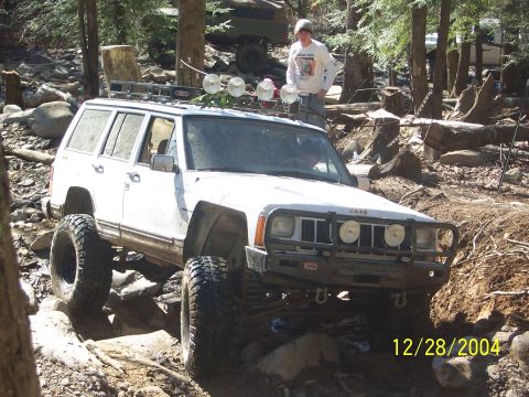 1987 Ford Bronco - A white Jeep Cherokee navigates a rocky trail, with another vehicle in the background.