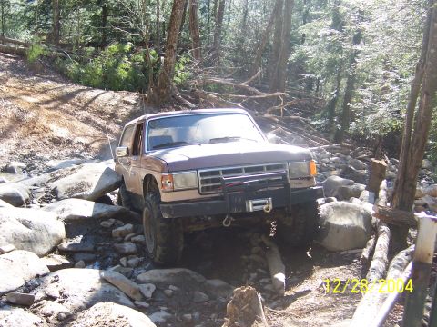 1987 Ford Bronco - This 1987 Ford Bronco is shown off-roading through a rocky stream, demonstrating its capability on challenging terrain.