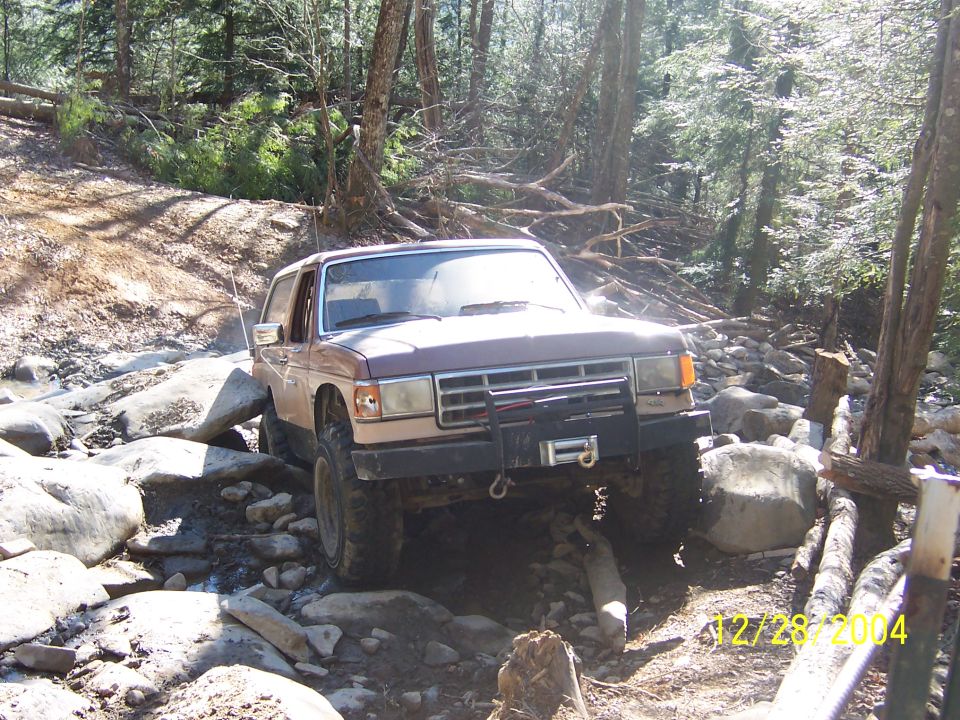 1987 Ford Bronco navigating rocky stream bed, front winch visible