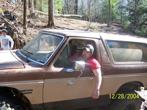 1987 Ford Bronco - A man poses in his Ford Bronco while off-roading in a wooded area. The vehicle appears to be stuck in mud.