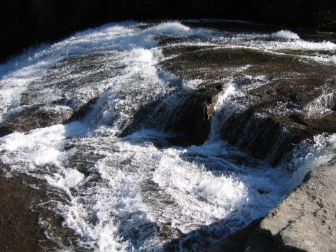 1985 Ford LTD Crown Victoria - A powerful waterfall flows over dark rocks, creating white foam and spray in the sunlight.