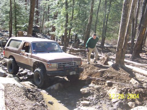 1987 Ford Bronco - 1987 Ford Bronco tackling a challenging off-road course in a wooded area.