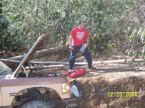 1987 Ford Bronco - A man stands by a 1987 Ford Bronco with its hood up, parked on a wooded trail.