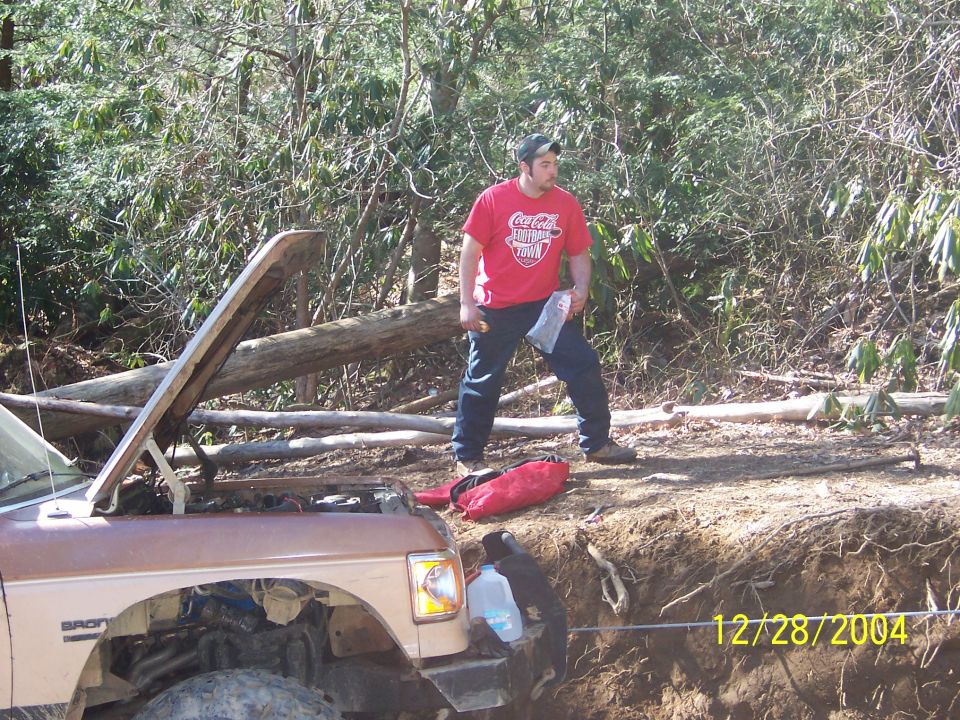 Brown 1987 Ford Bronco with hood open, parked on a dirt embankment with a man standing nearby
