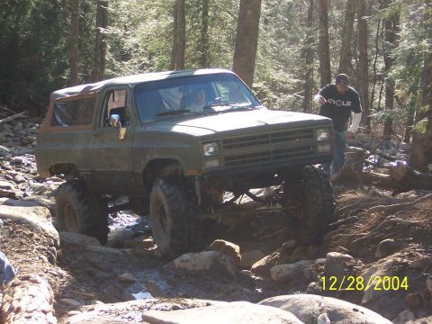 1987 Ford Bronco - Modified SUV tackling a challenging off-road course in a wooded area.