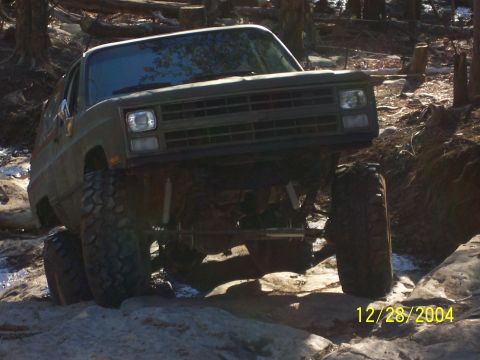1987 Ford Bronco - This SUV is shown off-roading on a rocky trail with trees in the background.