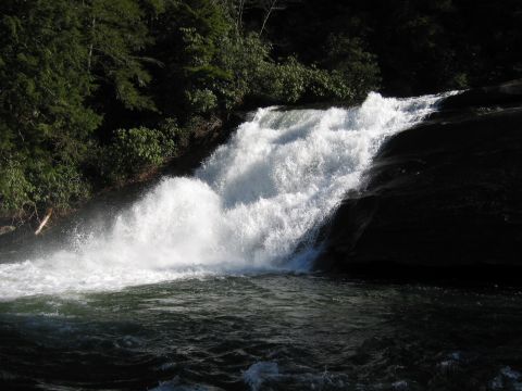 1985 Ford LTD Crown Victoria - A powerful waterfall flows over dark, smooth rocks, surrounded by dense green foliage.