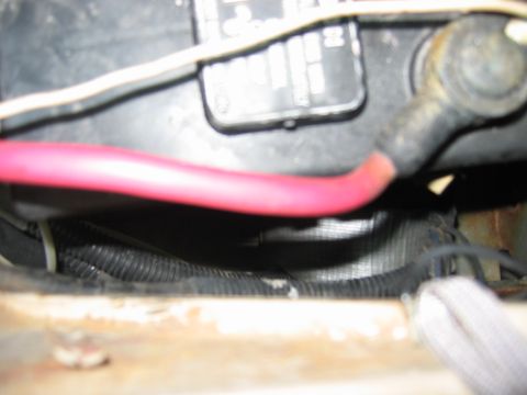 1985 Ford LTD Crown Victoria - Blurry close-up under the hood alongside a black battery case, with a heavy red positive battery cable running across the frame to a bolt t…