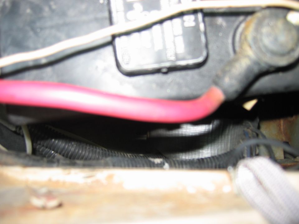 Close-up of red positive battery cable and wiring loom beside a black battery in an engine bay
