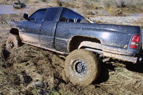 1994 Ford Bronco - This pickup truck is stuck deep in the mud, with another vehicle visible in the background water.