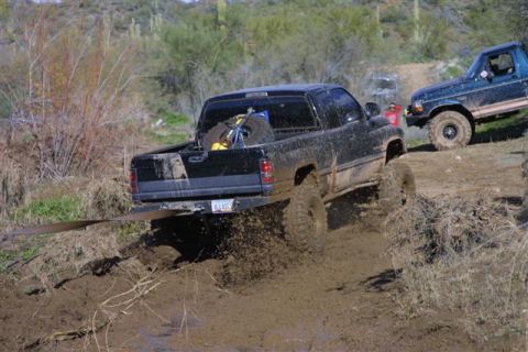 1994 Ford Bronco - Two trucks navigate a muddy off-road course, with one truck deeply stuck in the mire.