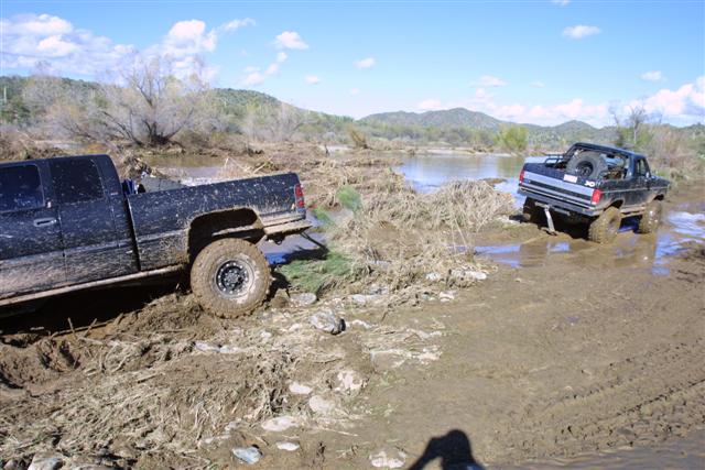 Two trucks stuck in mud and water, with a spare tire visible on the rear of one