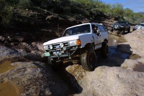 1994 Ford Bronco - White Ford Bronco off-roading on a rocky trail with other vehicles present.
