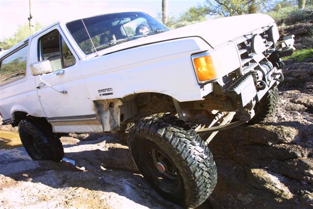 White Ford Bronco climbing over rocks on a trail. It has large off-road tires and a winch on the front