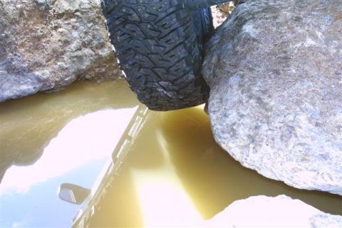 1994 Ford Bronco - This vehicle is navigating a challenging off-road obstacle with water and large rocks.
