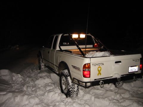 1985 Ford Bronco - A white Toyota Tacoma TRD Off-Road is parked in deep snow at night, equipped with off-road lights.