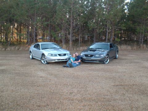 1999 Ford Mustang - A couple poses with two Ford Mustangs in an outdoor setting.