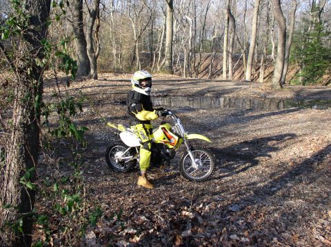 2000 Ford Excursion - A dirt bike and rider are positioned on a muddy trail surrounded by trees.
