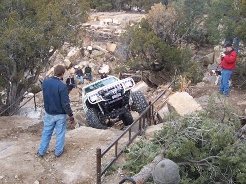 1991 Ford Bronco - A modified white off-road vehicle tackles a challenging rocky incline with spectators watching.