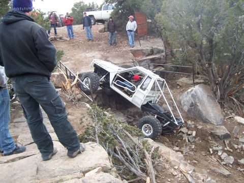 1991 Ford Bronco - A heavily modified off-road vehicle, likely not a 1991 Ford Bronco, tackles a challenging rocky trail with spectators watching.