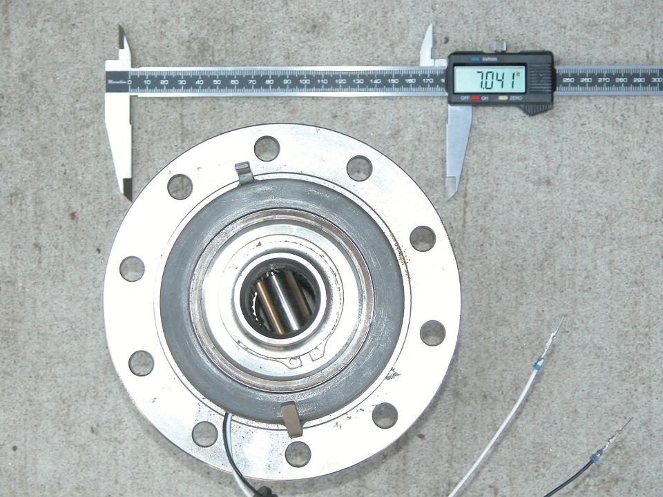 Disassembled axle hub flange with bearing measured by digital caliper reading 70.41 on concrete
