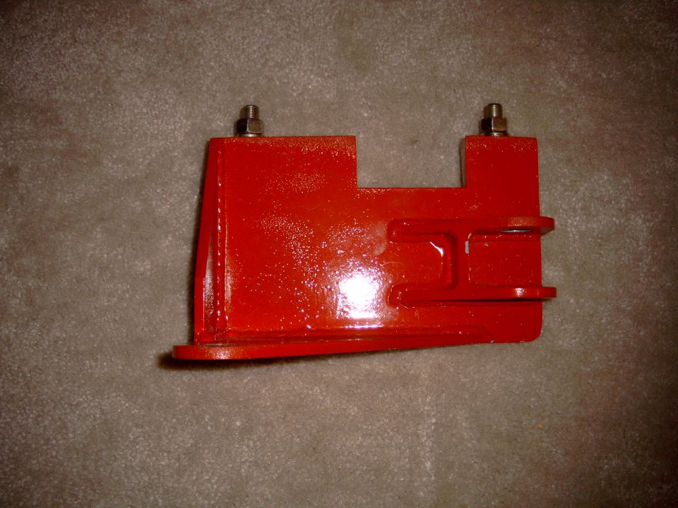 Red metal bracket with two bolts on top, resting on a carpeted surface