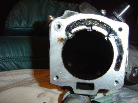 1998 Ford Taurus - A close-up view of a dirty throttle body, showing internal buildup and a visible part number on an attached hose.