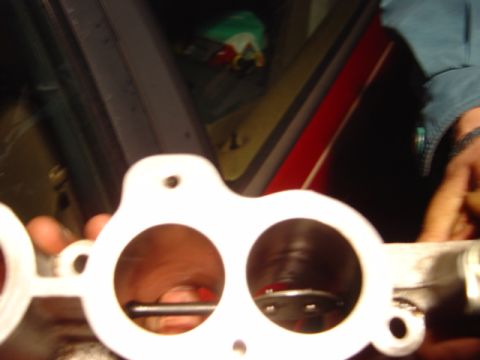 1998 Ford Taurus - A white intake manifold gasket is held in front of a red car's interior.