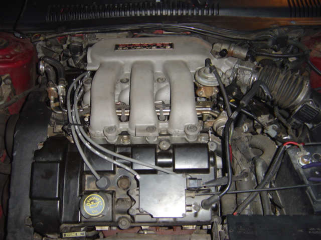 Engine bay with V6 engine components visible. Oil cap reads 'Engine Oil'