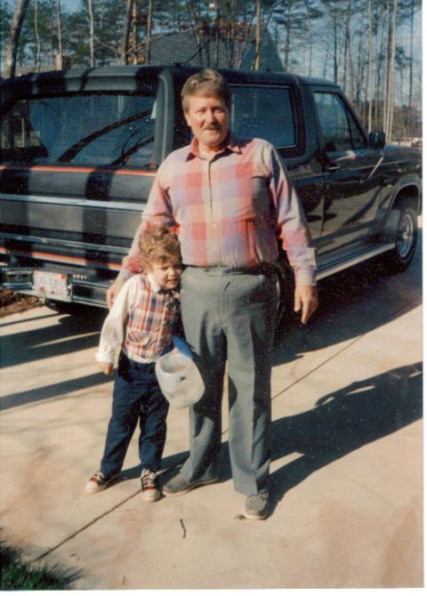 1985 Ford Bronco - A man and a young child pose for a photo in front of a dark-colored pickup truck.