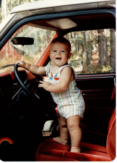 1985 Ford Bronco - A baby smiles while standing in the driver's seat of a 1985 Ford Bronco.
