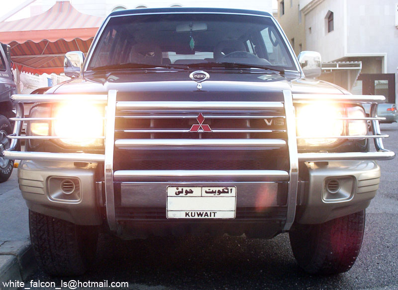 Dark Mitsubishi Pajero SUV, front view, headlights on, chrome grille guard, Kuwait plate