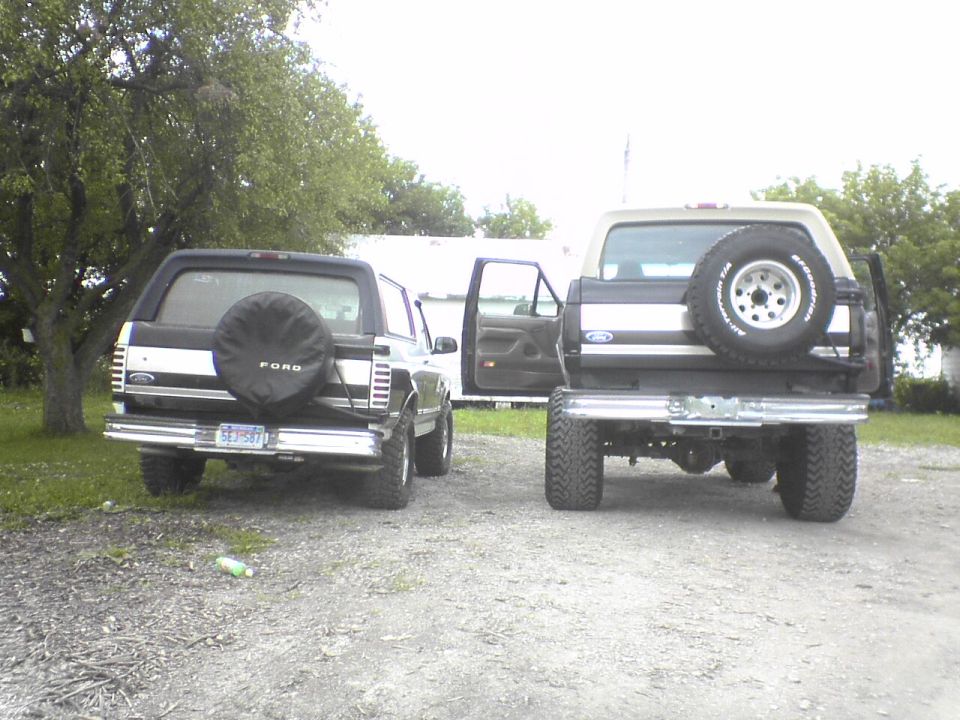 Two Ford Broncos parked side-by-side, both showing their rear ends. The one on the left has a spare tire cover with 'FORD' on it. The one on the right has its spare tire mounted externally