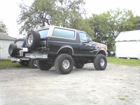1995 Ford Bronco - A lifted black and tan Ford Bronco with flame decals is parked next to another vehicle.