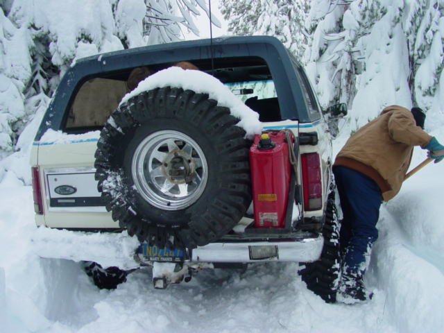 1986 Ford Bronco with spare tire and gas can in snow, person shoveling