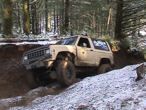 1994 Ford Explorer - This off-road SUV, likely a Ford Bronco II from the late 1980s, is shown traversing a challenging trail in a wooded area.