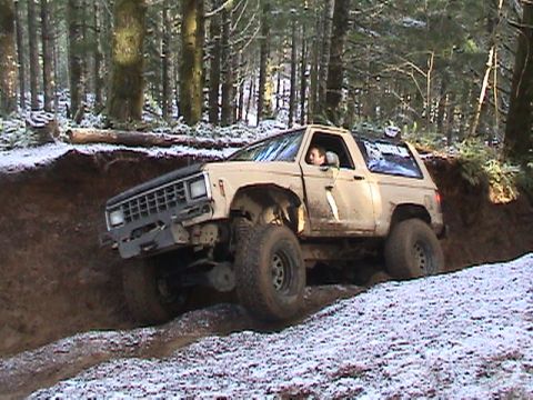 1994 Ford Explorer - A tan off-road SUV with large tires is seen navigating a muddy incline in a forest setting.